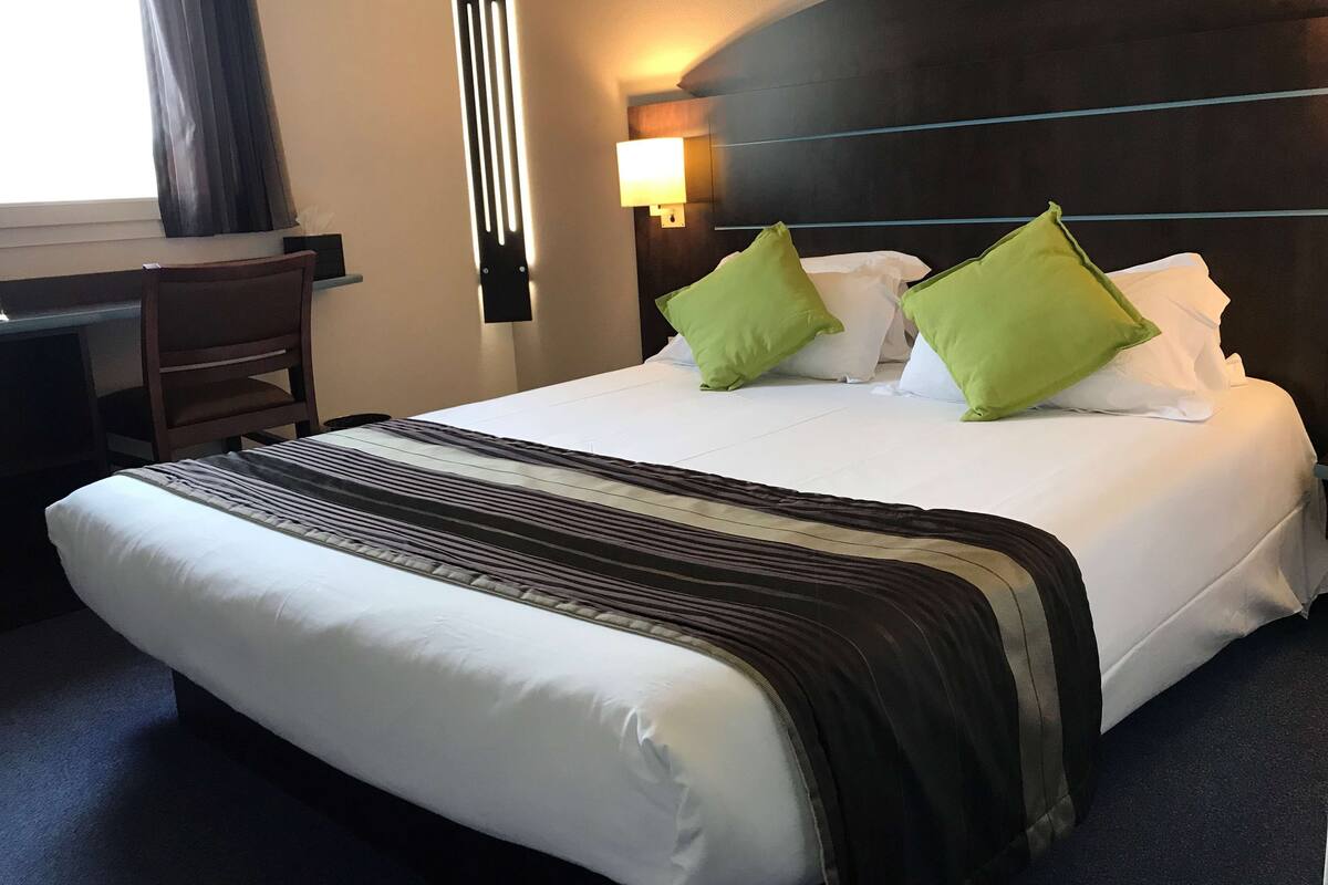 A hotel room with a large bed, a desk, and a chair.