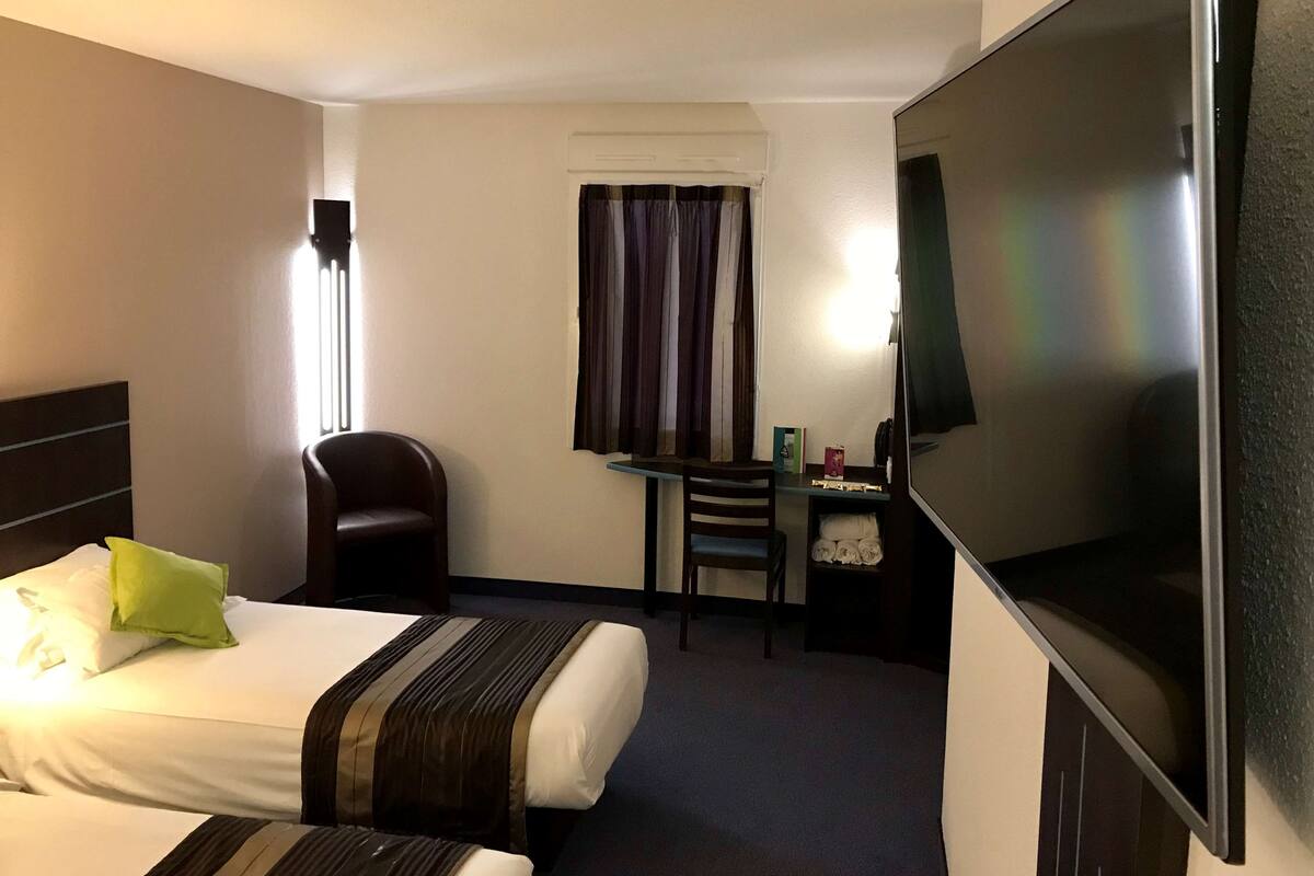 A hotel room with a bed, a desk, a chair, a TV, and a window with curtains.