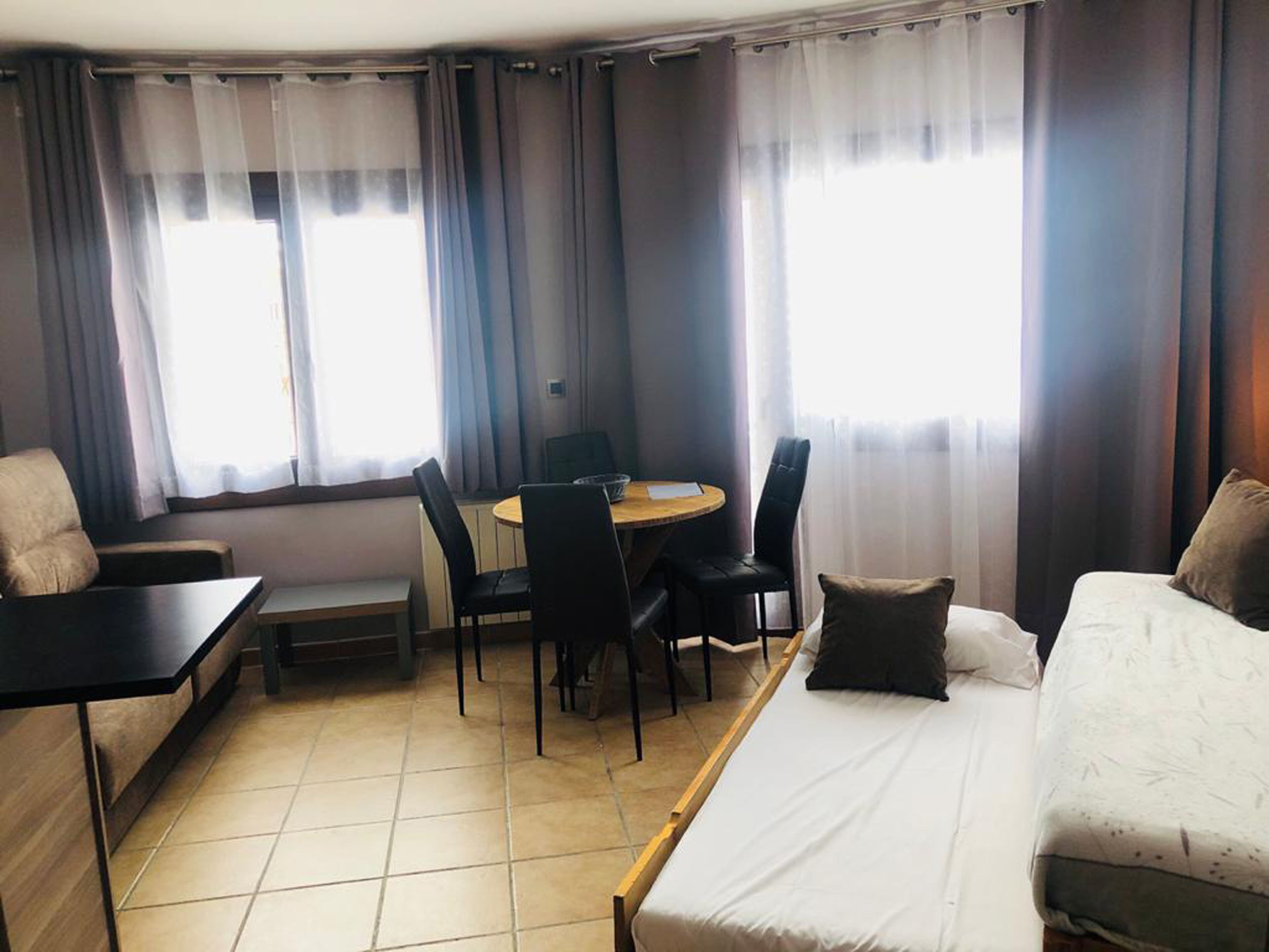 Een hotelkamer met een bed, een bureau en een stoel. Er hangen gordijnen voor de ramen.