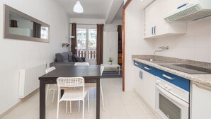 A modern kitchen with white cabinets, a granite countertop, and a built-in oven. There is a dining area with a dark wooden table and white chairs.