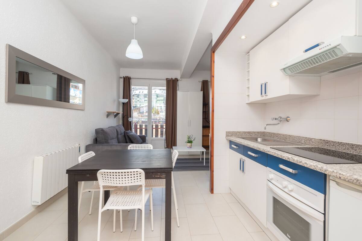 A modern kitchen with white cabinets, a granite countertop, and a built-in oven. There is a dining area with a dark wooden table and white chairs.