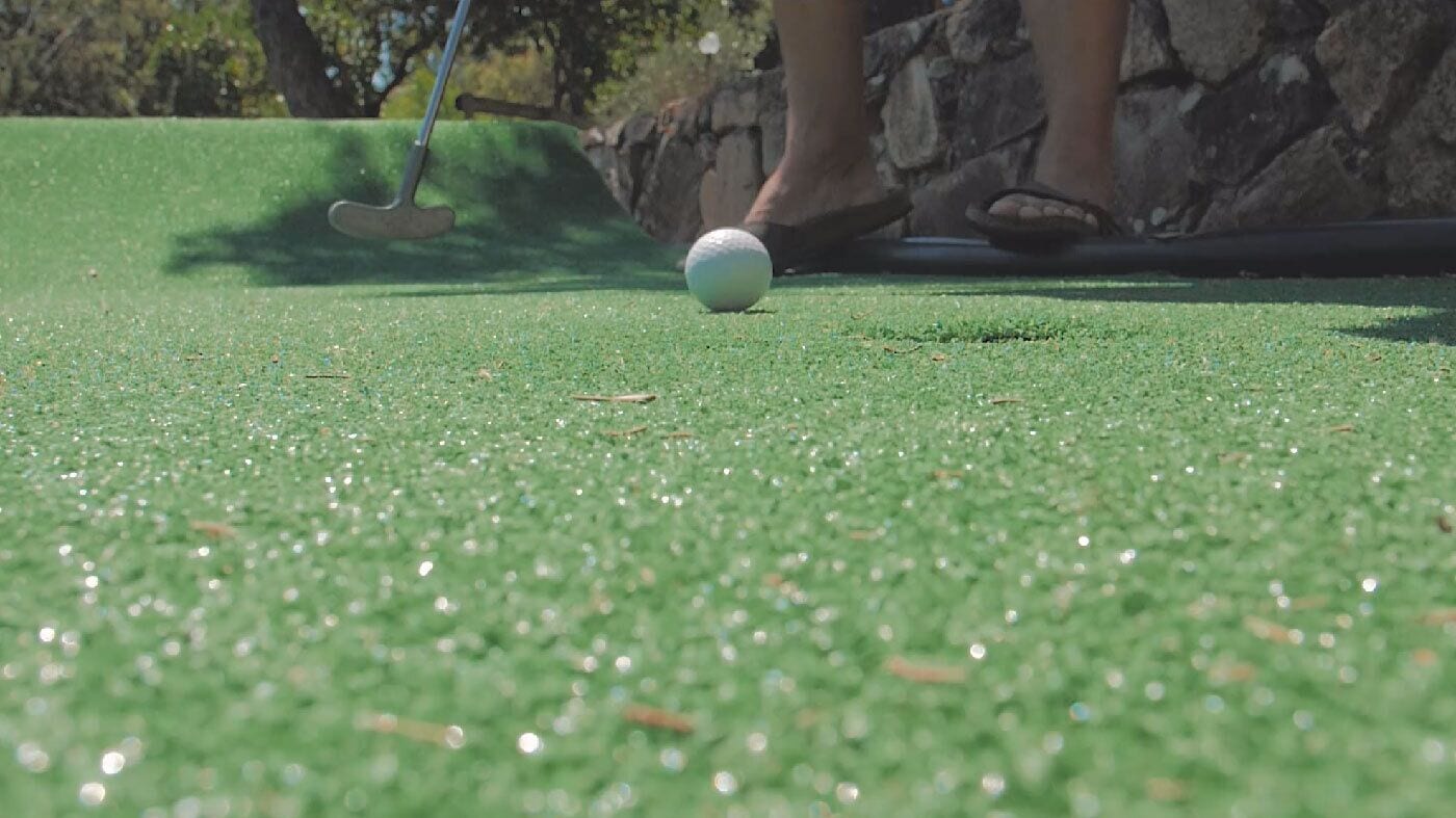 A golf ball on a green with a putter nearby.