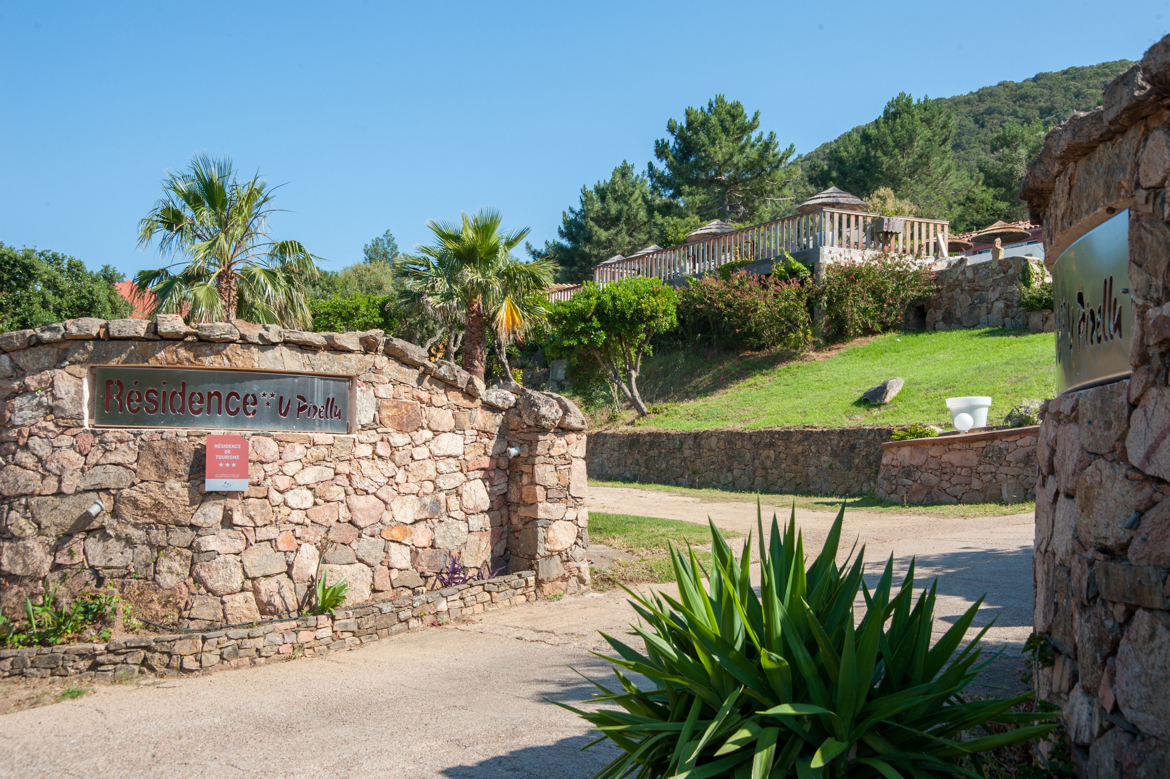 A stone wall with a sign reading "Residence U Pinella" and a pathway leading to a building with a dome structure.