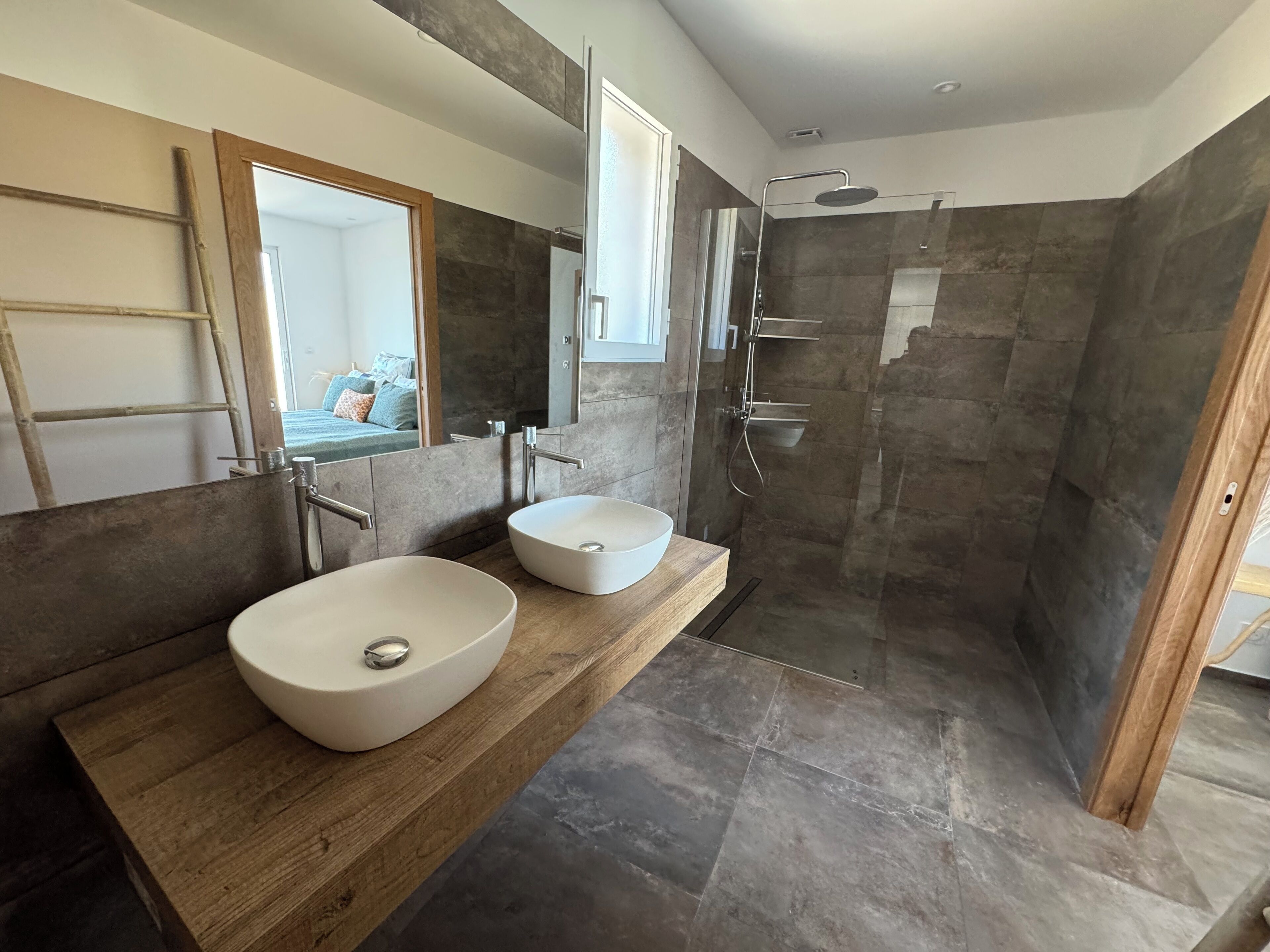 Un baño moderno con dos lavamanos grandes, una ducha a ras de suelo y un mueble de tocador de madera.