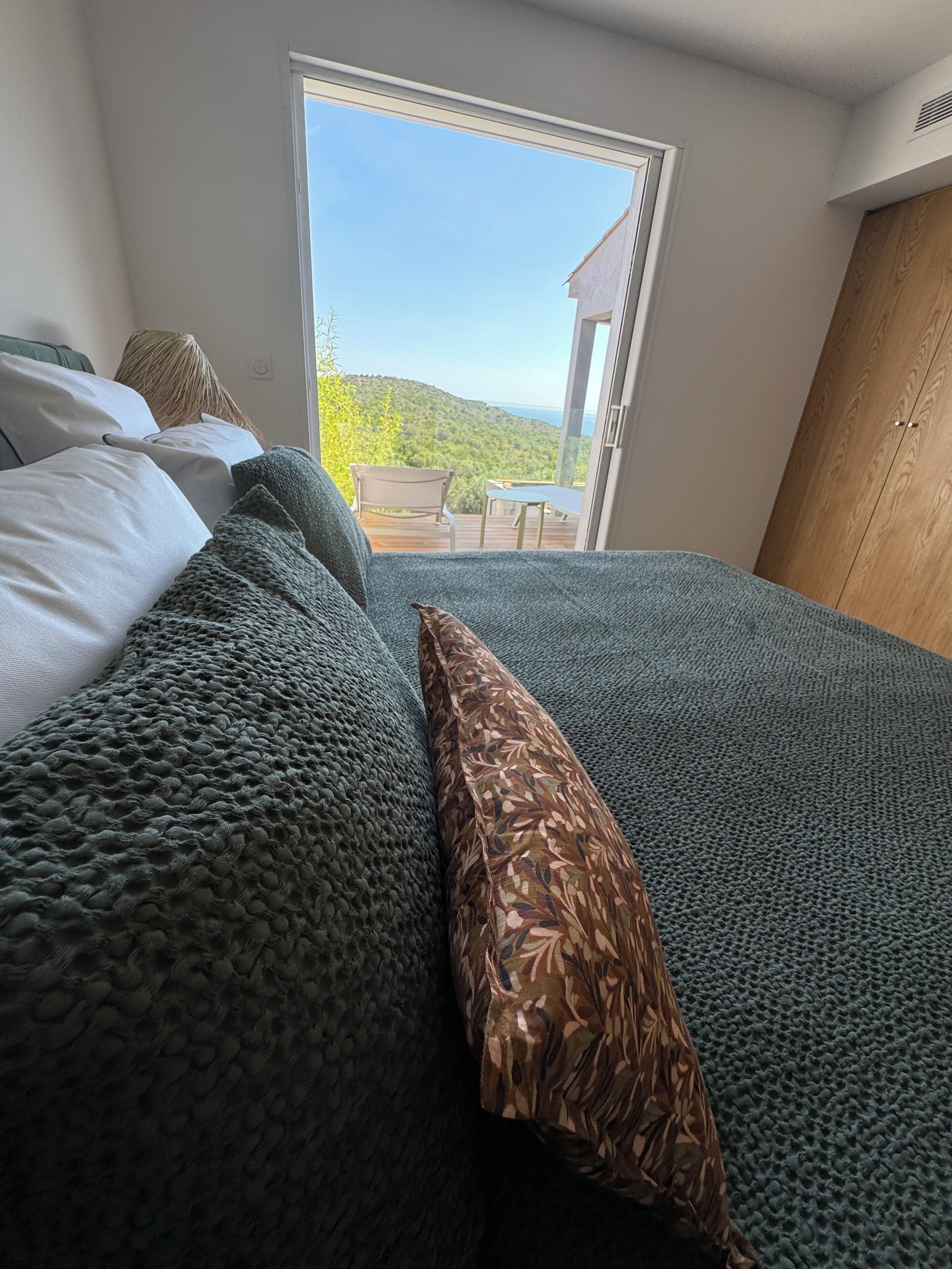 Een slaapkamer met een groot bed, een houten kledingkast en uitzicht op een heuvel door een glazen deur.