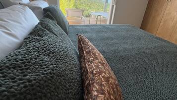 Een slaapkamer met een groot bed, een houten kledingkast en uitzicht op een heuvel door een glazen deur.