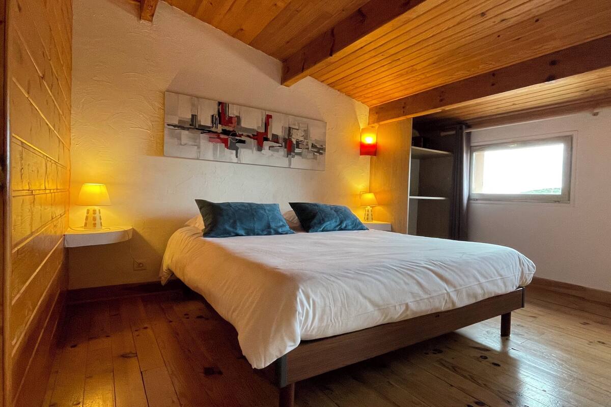 Ein Schlafzimmer mit Holzboden, einem Bett mit weißer Bettwäsche, zwei blauen Kissen und zwei Nachttischlampen.