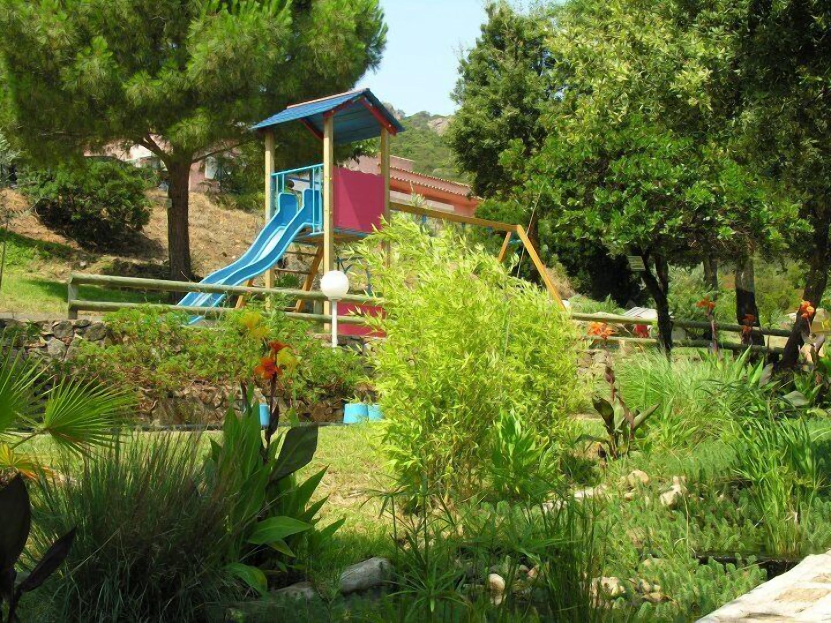 Un parque infantil con tobogán y estructuras para escalar, rodeado de abundante follaje y árboles.