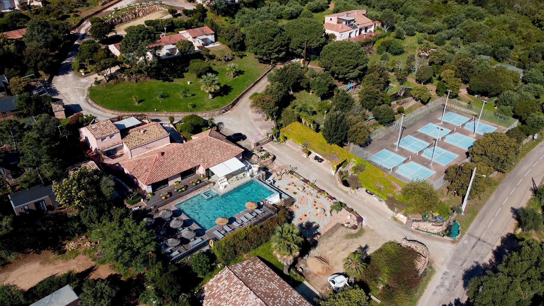 Vista aérea de una zona residencial con piscina, canchas de tenis y abundante vegetación.