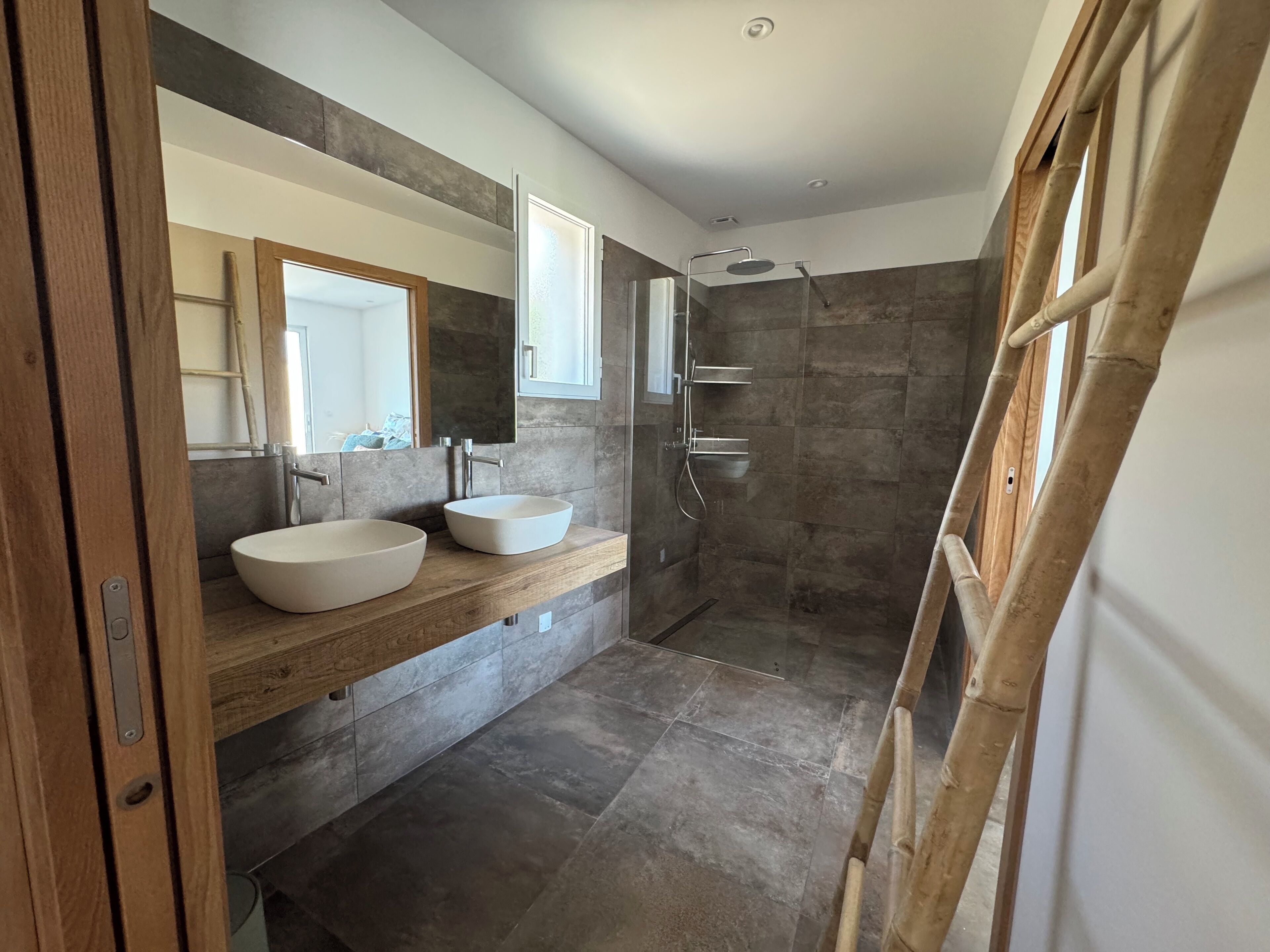 Un baño moderno con dos lavamanos, un espejo grande y una zona de ducha.