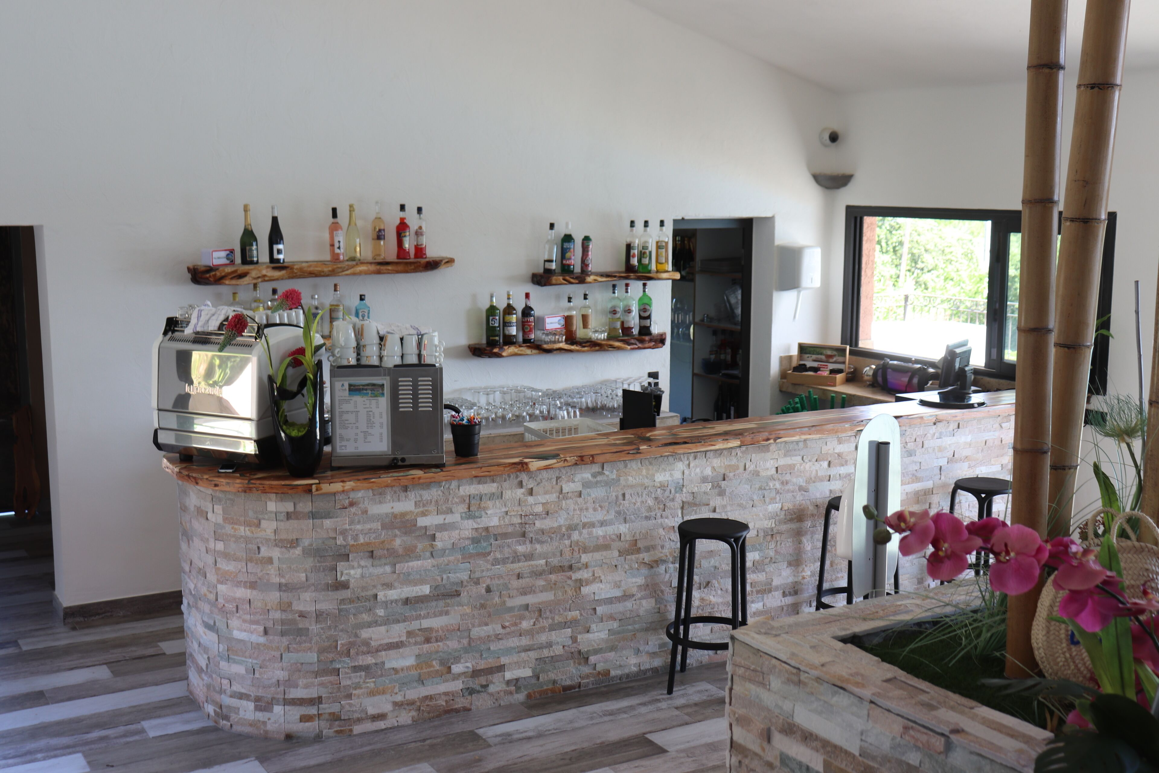 Un área de bar moderna con mostrador de piedra, diversas botellas de licor y una zona de estar con taburetes.