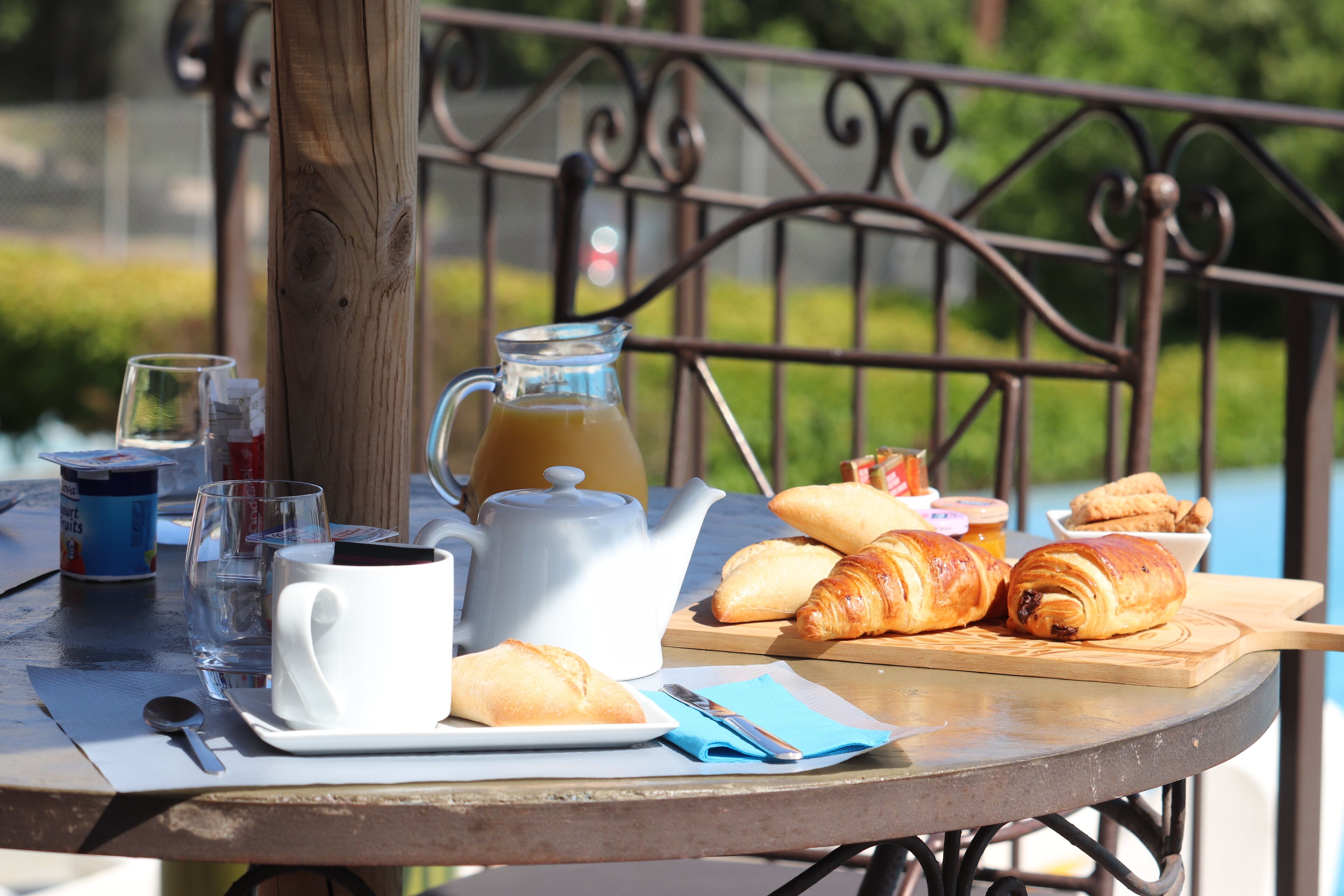 A table set with a white mug, a glass of water, a teapot, croissants, and a jug of juice.