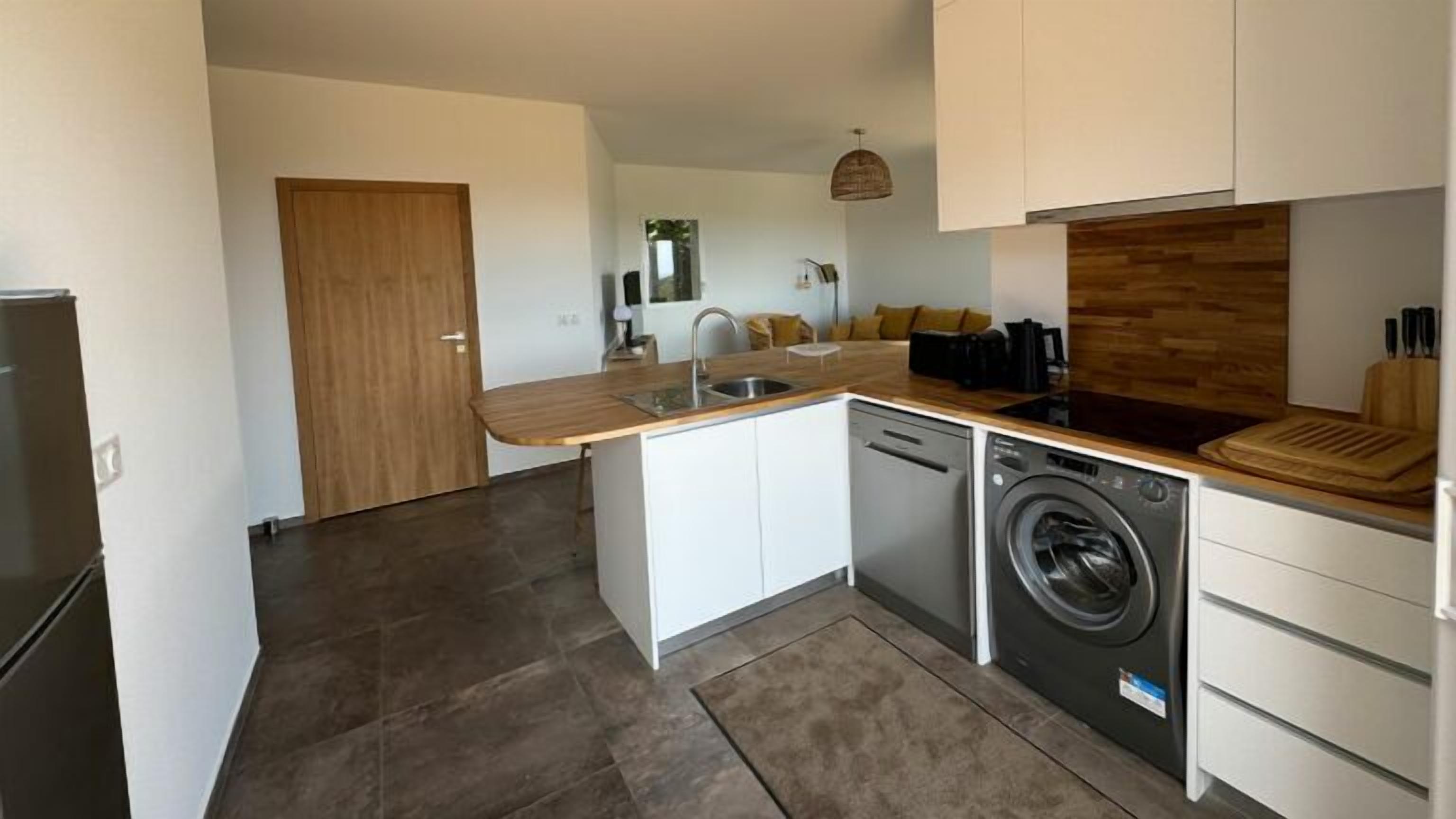 Une cuisine compacte équipée d’un lave-linge intégré, d’un évier et d’un plan de travail en bois.