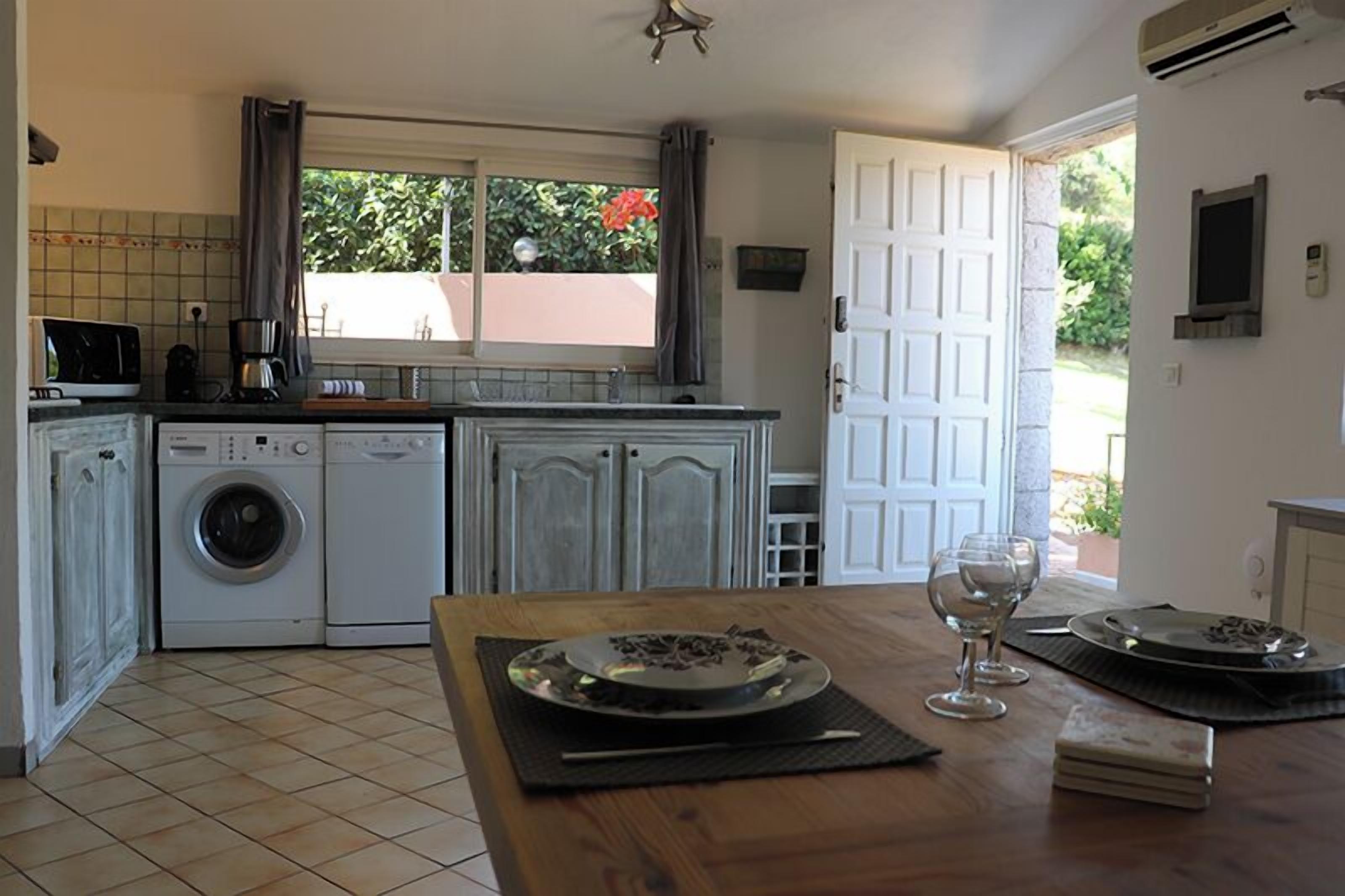 A kitchen with a washing machine, a coffee maker, and a dining table with a plate and wine glass.