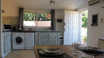 A kitchen with a washing machine, a coffee maker, and a dining table with a plate and wine glass.