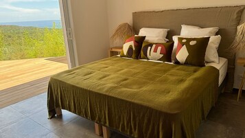 A bed with a green bedspread, a view of the outdoors, and a wooden floor.