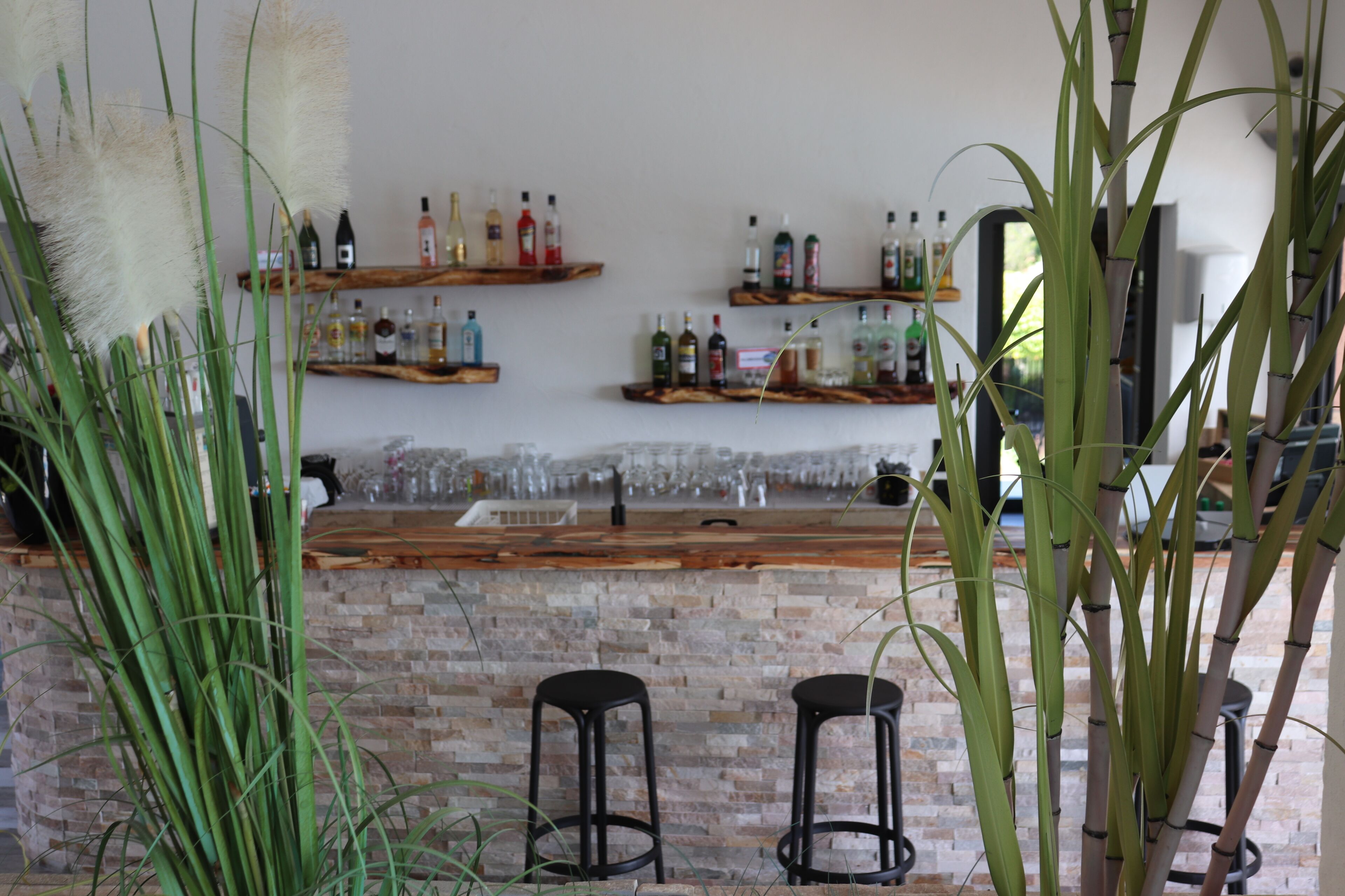 A bar area with a brick wall, shelves with bottles, and two black bar stools.