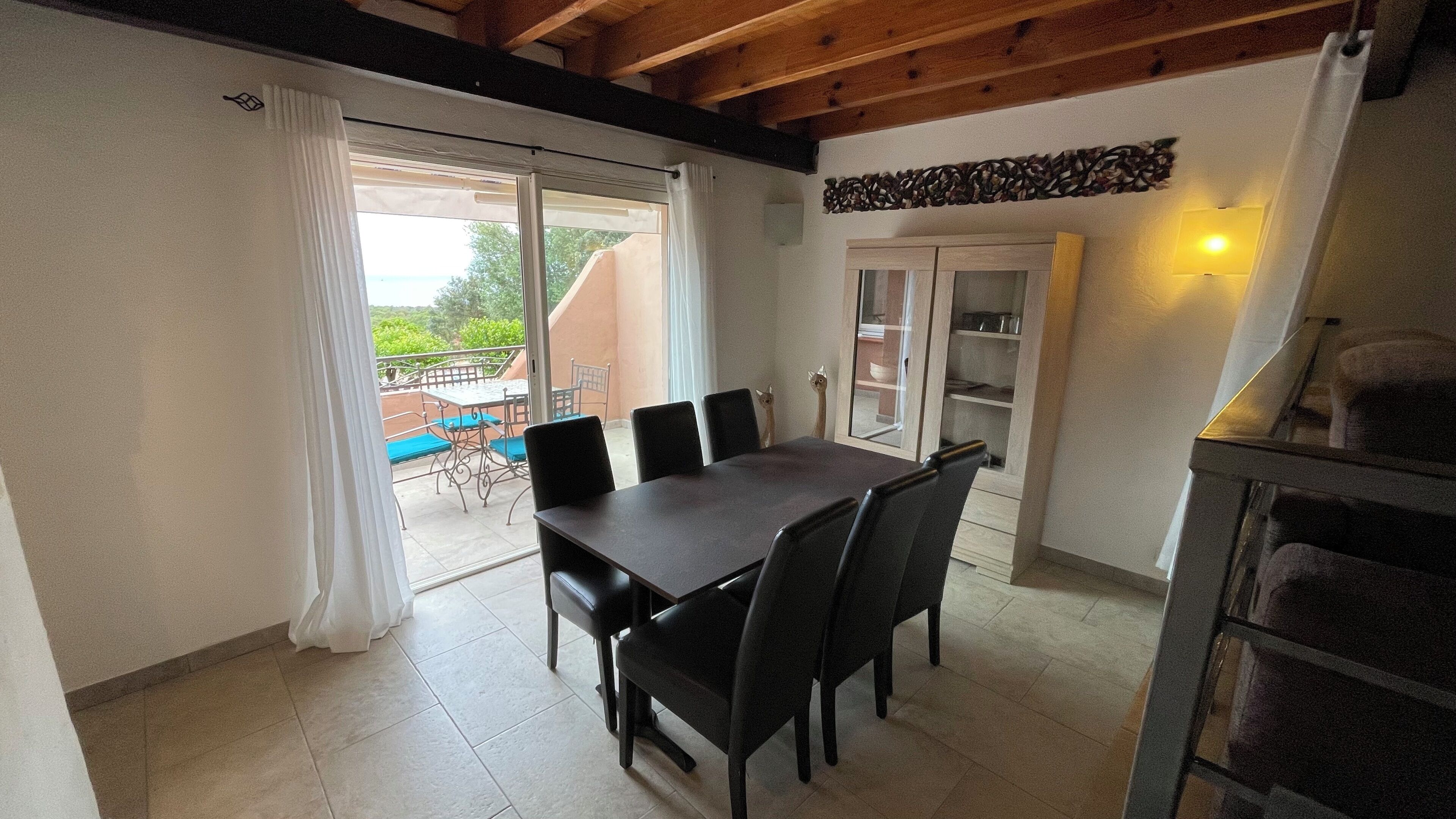 Un coin repas avec une table et des chaises, une porte-fenêtre coulissante donnant sur une terrasse extérieure et un meuble avec des portes en verre.