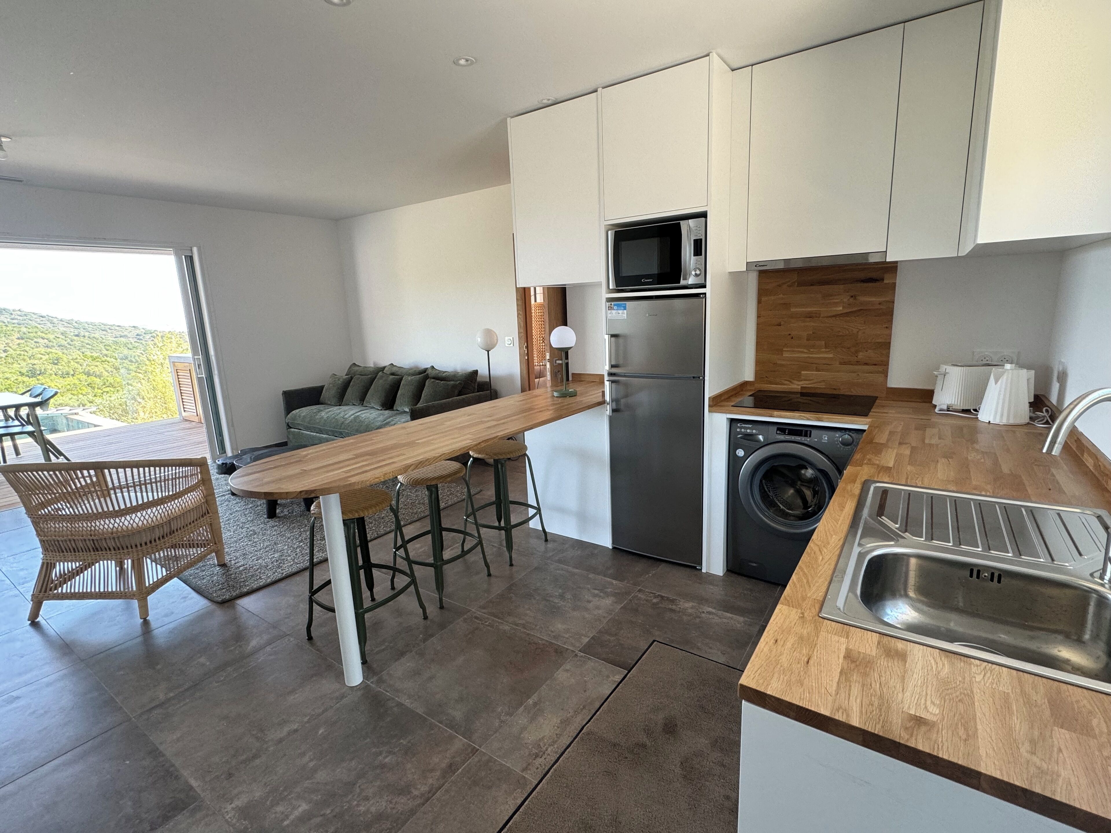 A modern kitchen with a wooden bar, stainless steel appliances, and a view of the outdoors.