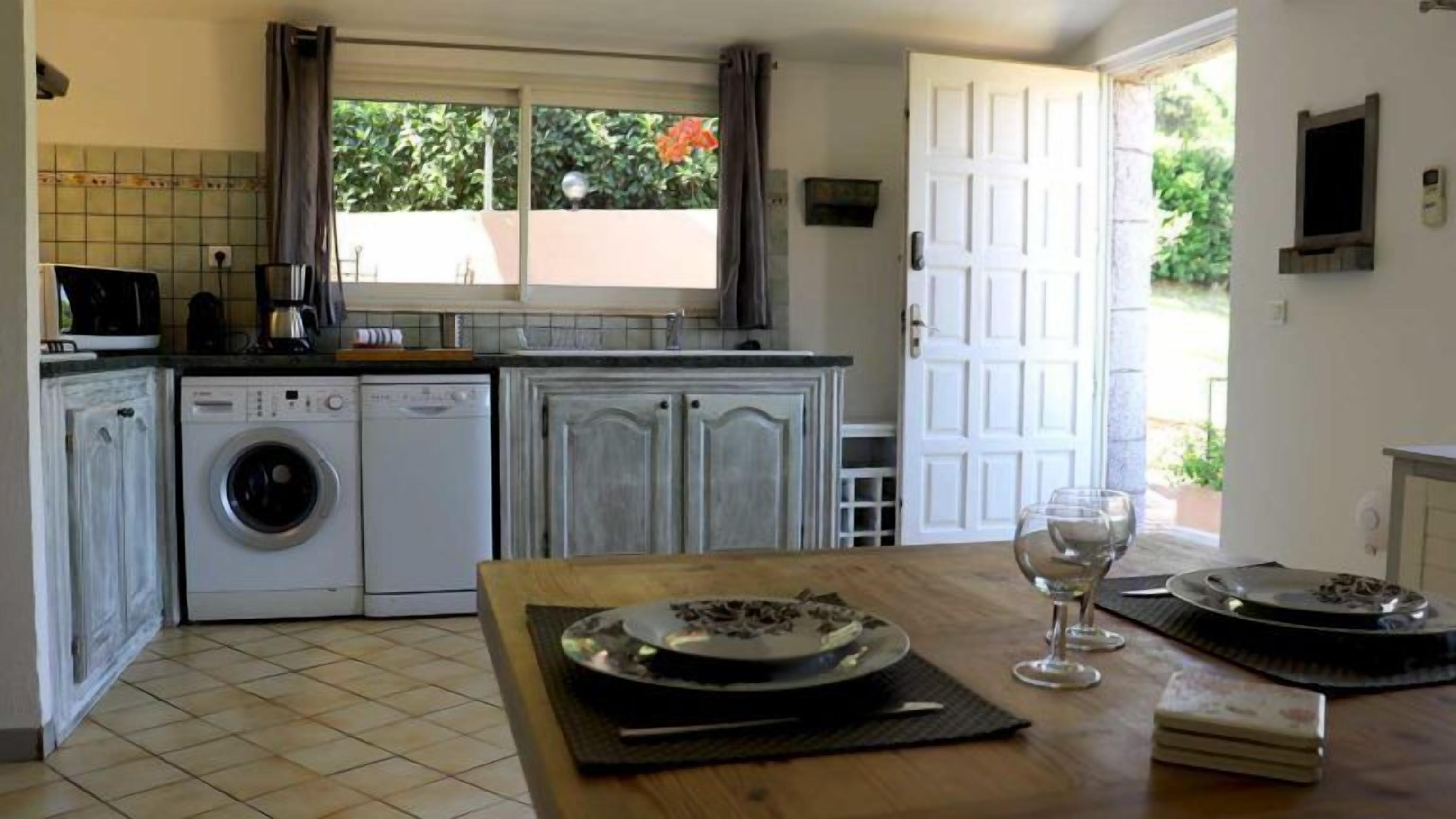 A compact kitchen with a washing machine, a sink, and a dining area with a table set for two.