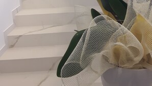 Una escalera con escalones de mármol blanco y barandilla de metal, que conduce a un rellano con pared blanca y una lámpara.