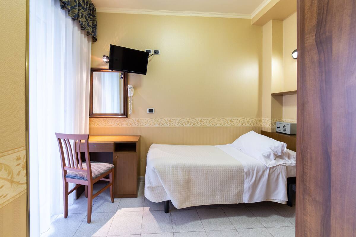 Habitación de hotel con cama, escritorio, silla, televisor y teléfono.
