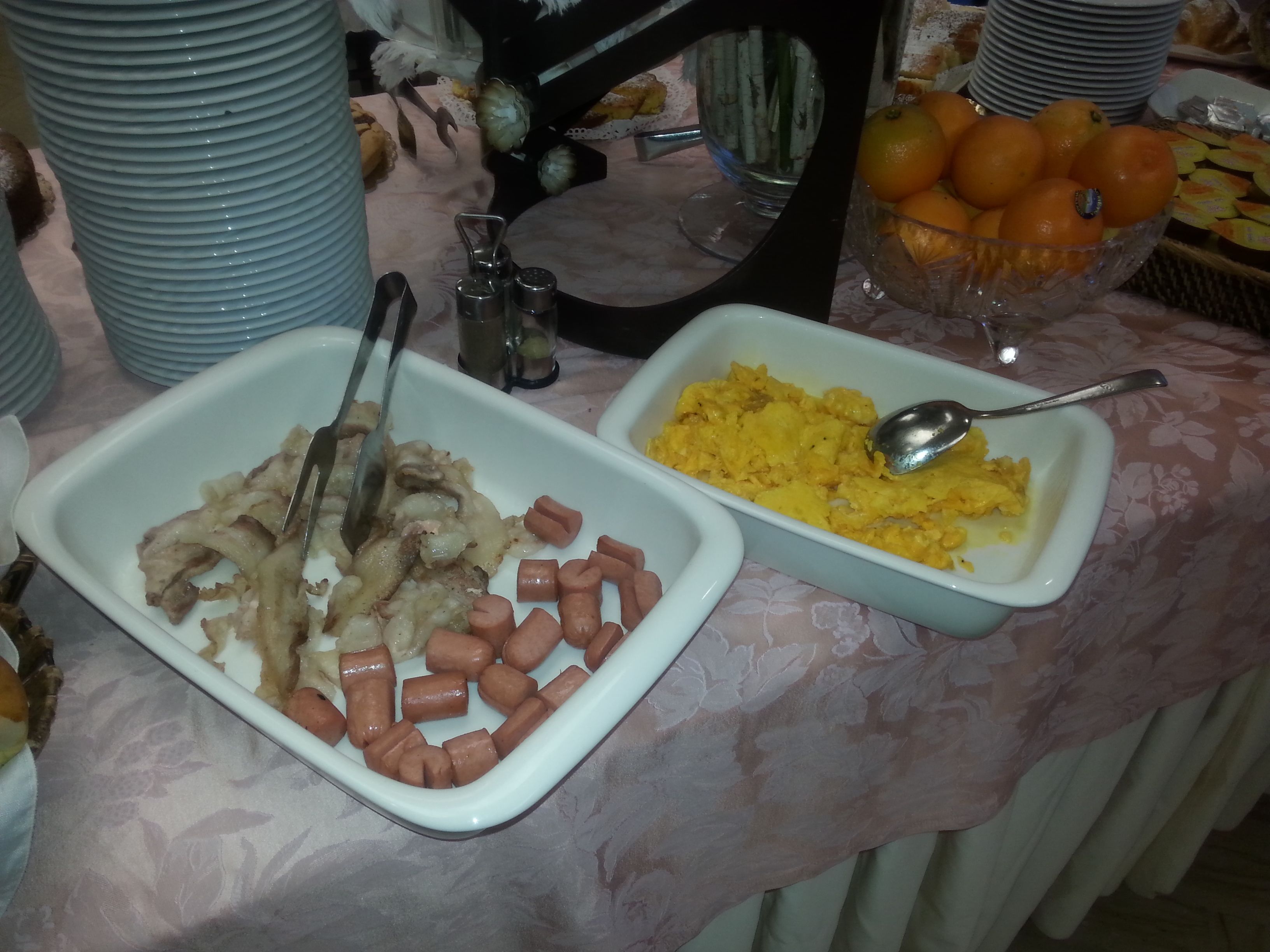 Una mesa de buffet con platos que incluyen salchichas y huevos revueltos.