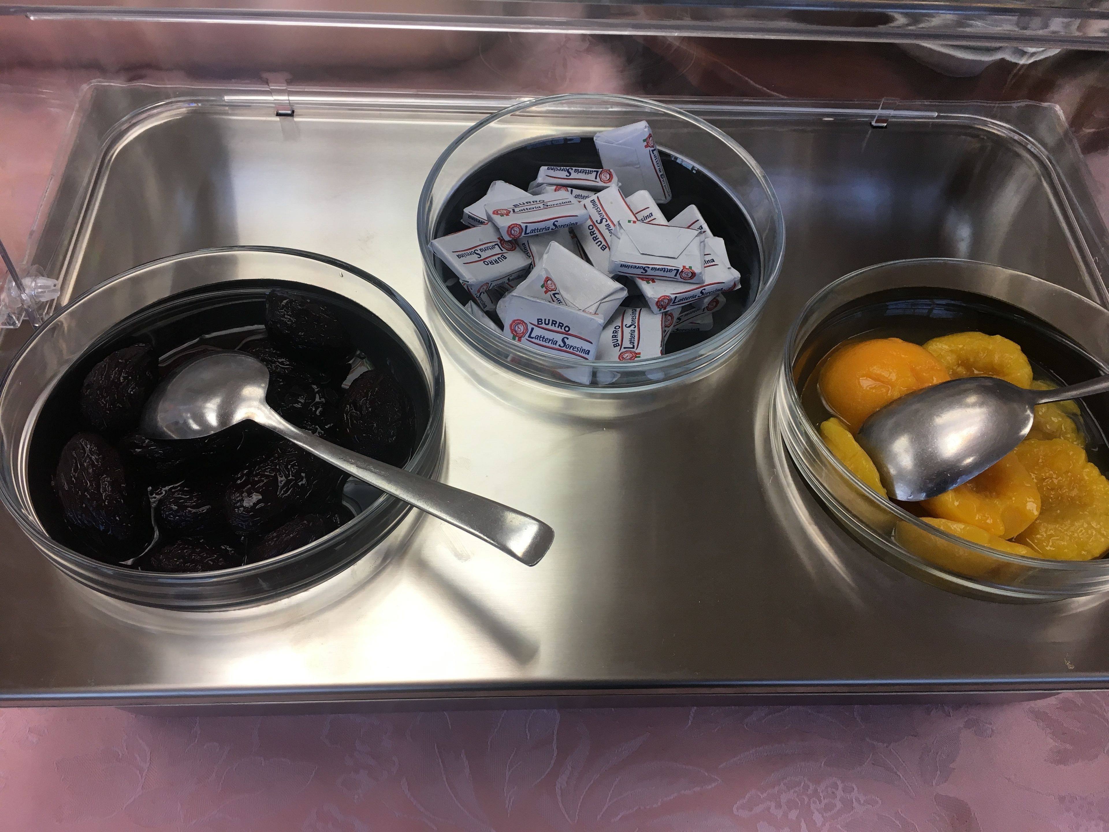 Un plateau en acier inoxydable contenant trois bols remplis de différents aliments, et une cuillère est fournie avec chaque bol.