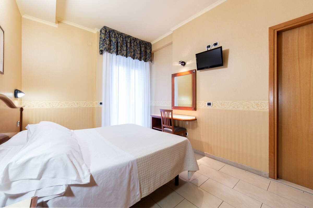 Una habitación de hotel con una cama, un escritorio, una silla, un televisor y una puerta de madera.