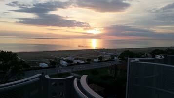 A coastal view with a sunset, a pier, and a road leading to a beach area.