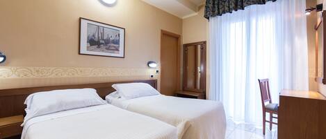 Habitación de hotel con dos camas, un escritorio de madera, una silla, un cuadro en la pared y una ventana con cortinas.