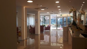 Un moderno vestíbulo de hotel con separador de vidrio, asientos rojos y vista al área exterior.
