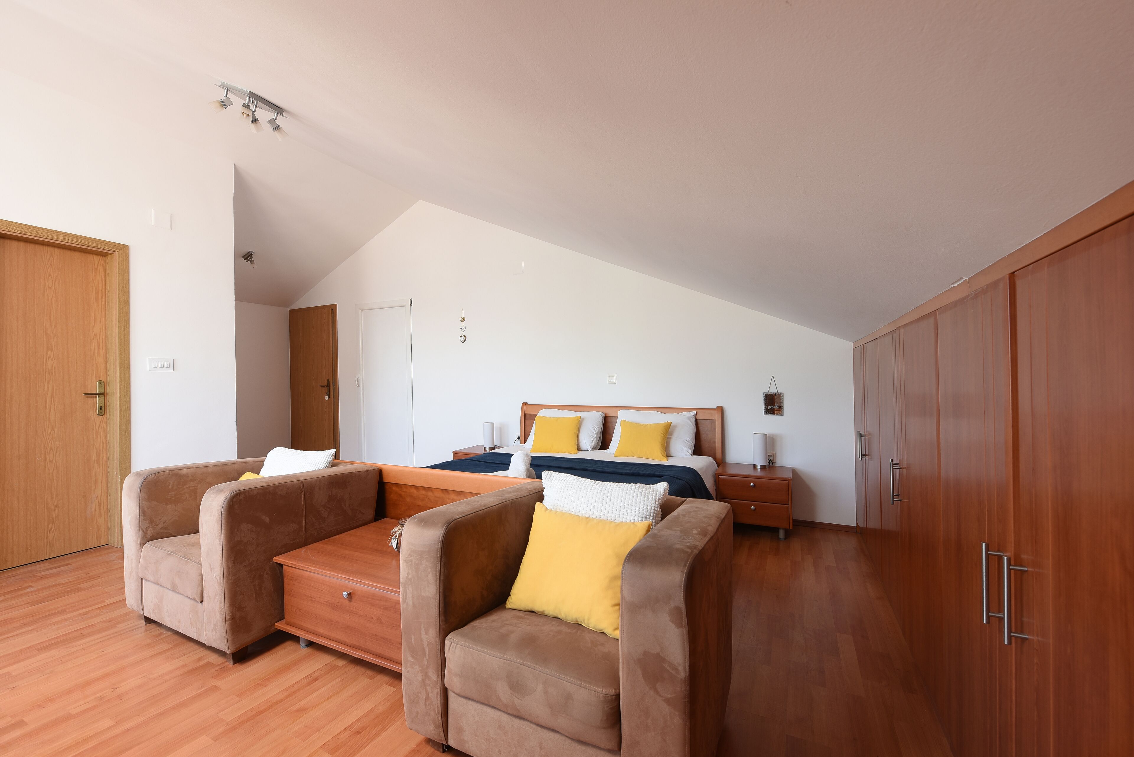 Une chambre à coucher avec un lit, une armoire en bois et deux fauteuils.