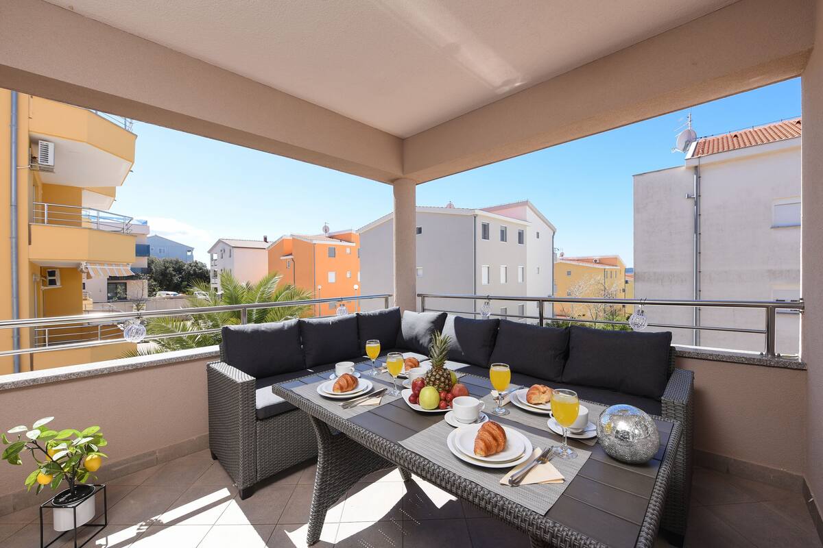 A balcony with a dining table set for breakfast, including croissants, fruit, and orange juice.