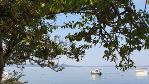 A rocky beach with lounge chairs and a calm sea with boats in the distance. - Sunset Beach Suites (Zadar)