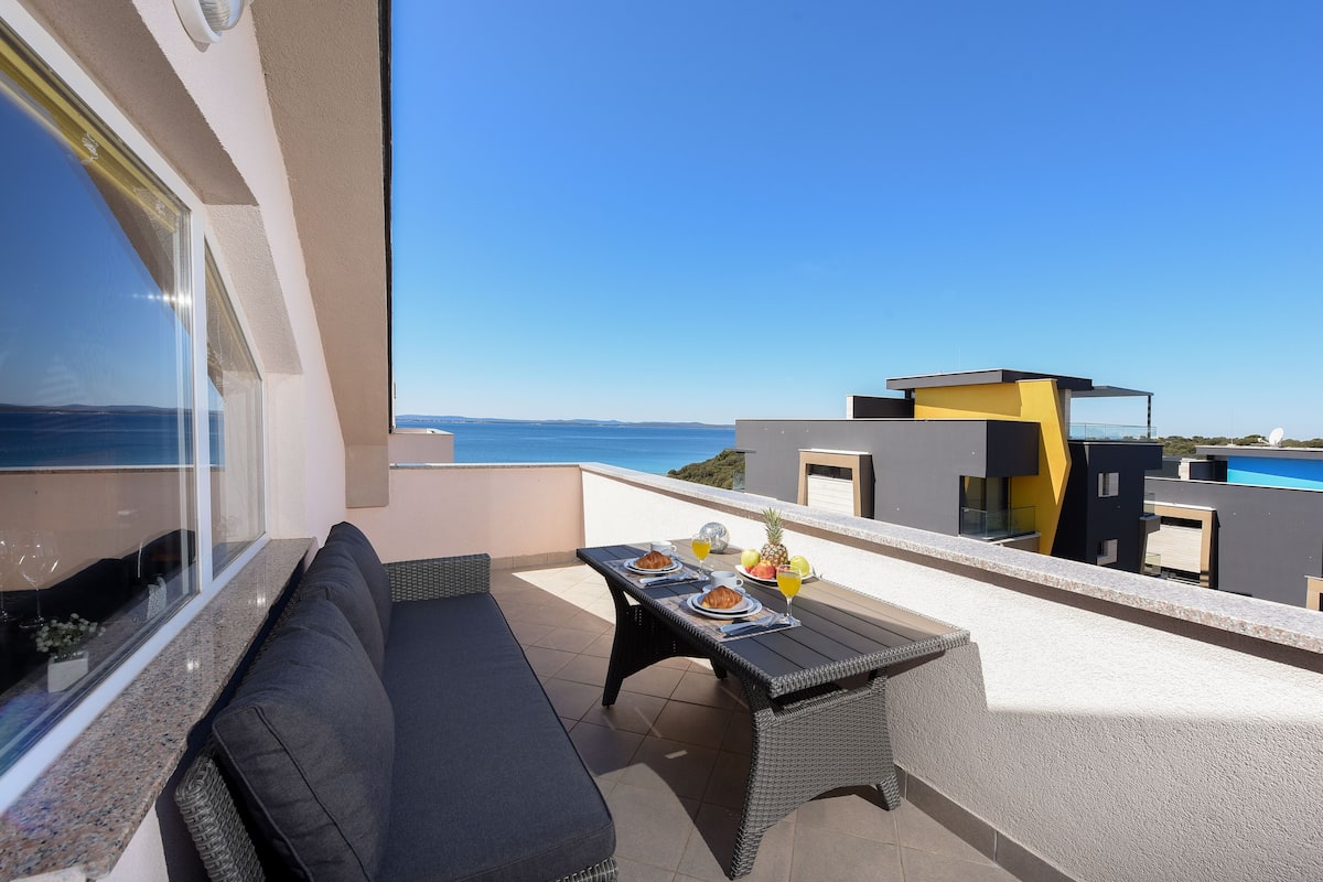 A balcony with a sofa, dining table, and a view of the sea.