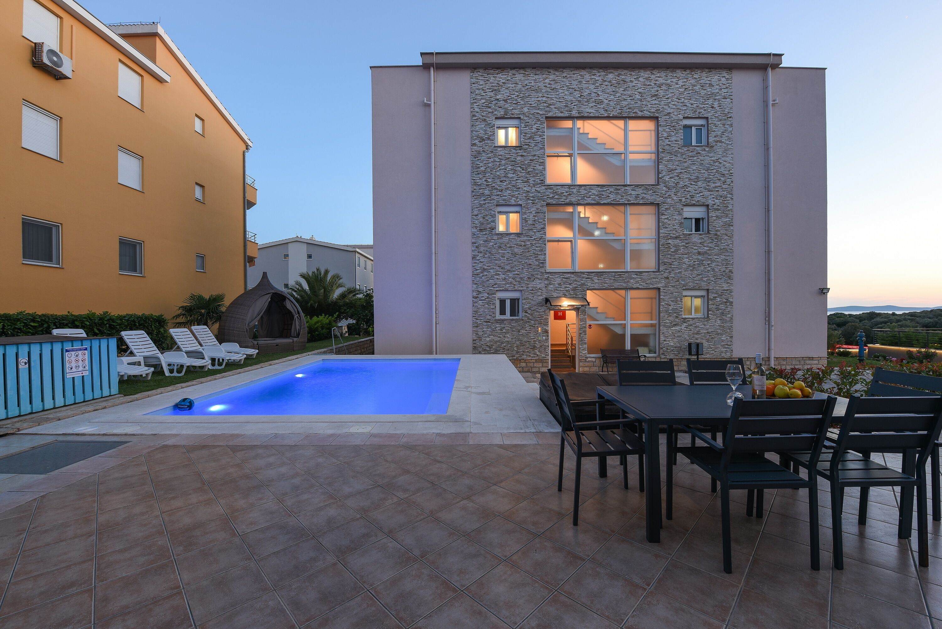 A modern building with a swimming pool, outdoor seating, and a stone facade.