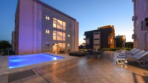 A modern outdoor pool area with a stone building, lounge chairs, and a dining area. - Sunset Beach Suites (Zadar)