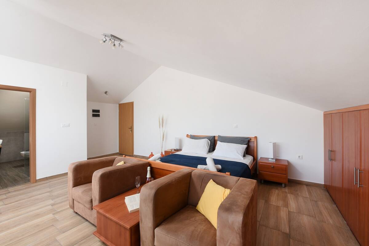 A modern bedroom with a bed, two sofas, a nightstand, and a wardrobe.