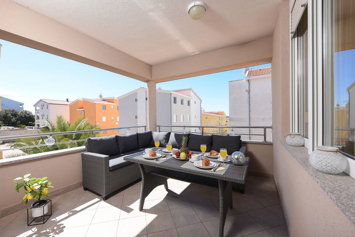 A balcony with a dining table set for breakfast, a sofa, and a potted plant.