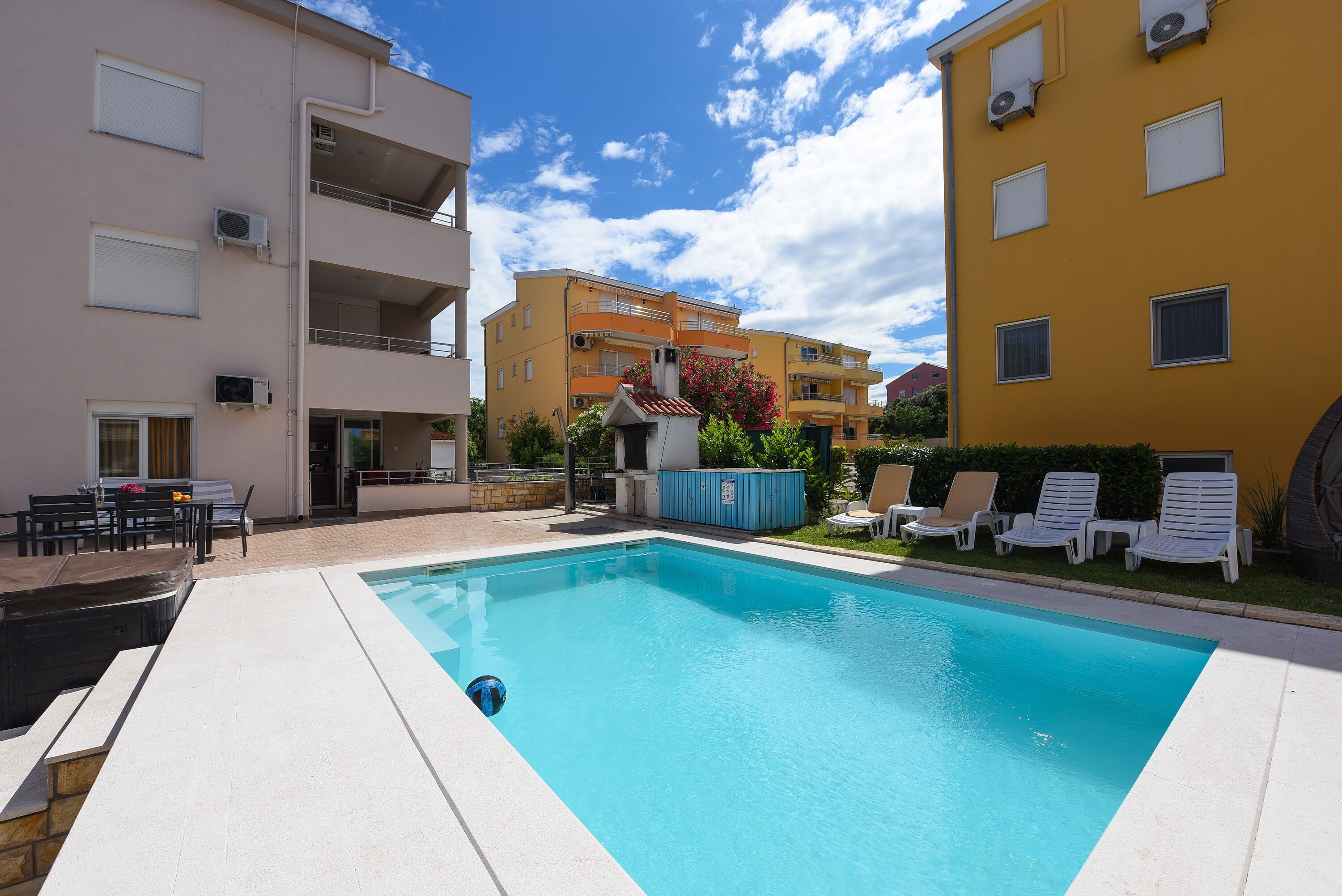 Une piscine avec des chaises longues, un petit jardin et un bâtiment doté de balcons.
