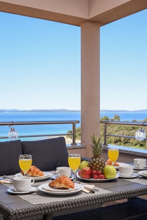 A breakfast table with croissants, fruit, and juice, overlooking a scenic view. - Sunset Beach Suites (Zadar)