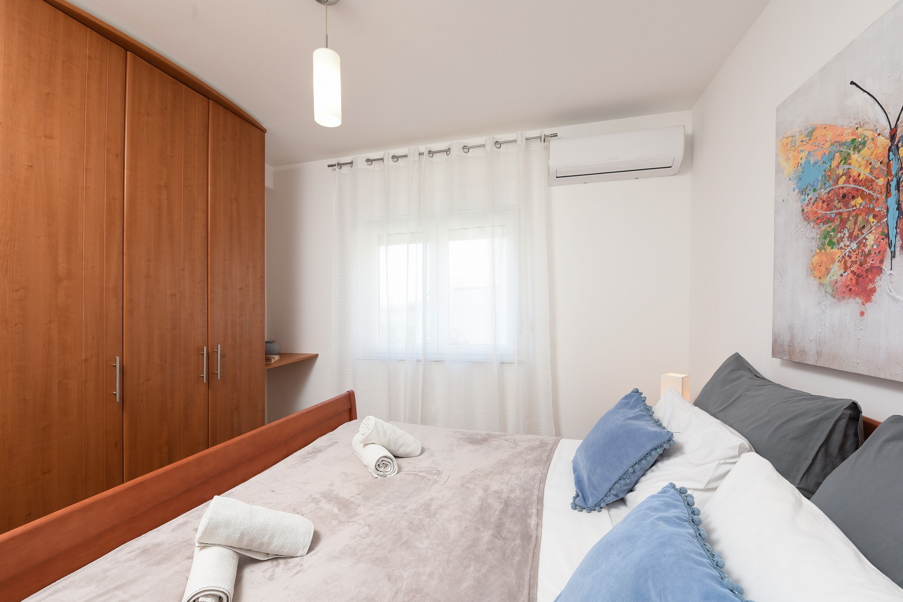 A neatly made bed with a white and blue duvet, a wooden wardrobe, and a map artwork on the wall.