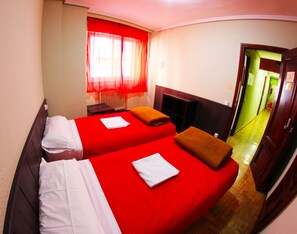 A hotel room with two beds, red bedding, a wooden headboard, a window with red curtains, and a wooden floor. - Hostel Escapa2 (Salamanca)