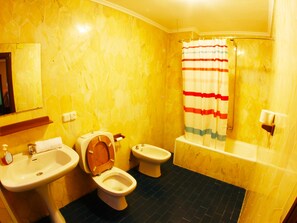 A bathroom with yellow hexagonal tiles, a wooden toilet, a bidet, a sink, and a shower with a striped curtain. - Hostel Escapa2 (Salamanca)