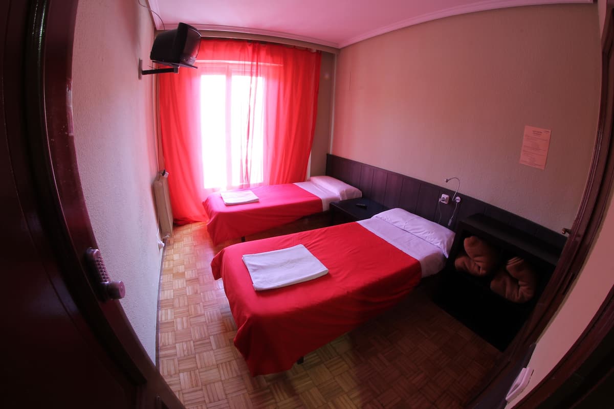 A room with two beds, a television, and a window with red curtains.