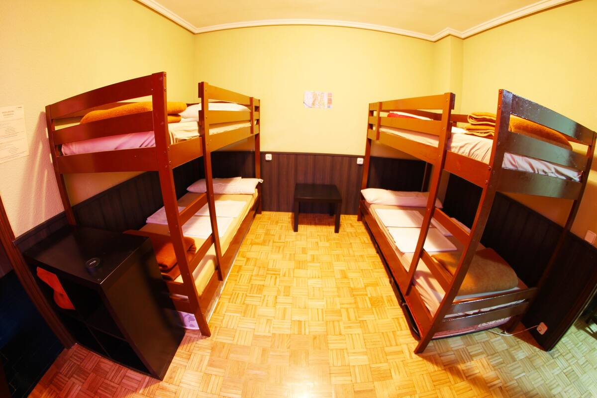 A room with three bunk beds, a small table, and a wall-mounted shelf.