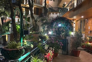 An indoor atrium with multiple levels, featuring a central staircase, various potted plants, and a decorative archway. - Hotel Mongas (Dalhousie)