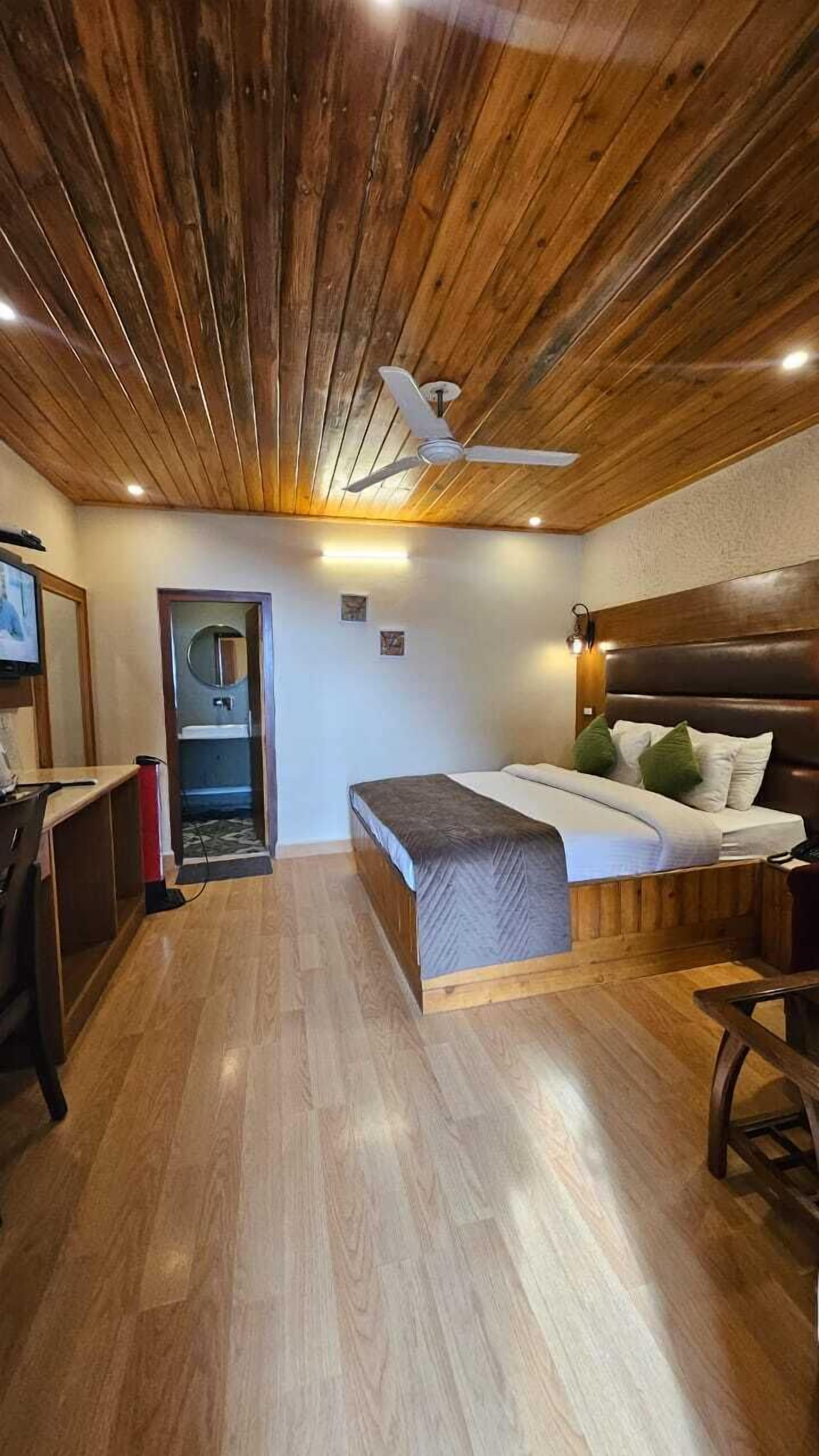 A room with a wooden ceiling, a bed with pillows, a desk, and a chair.