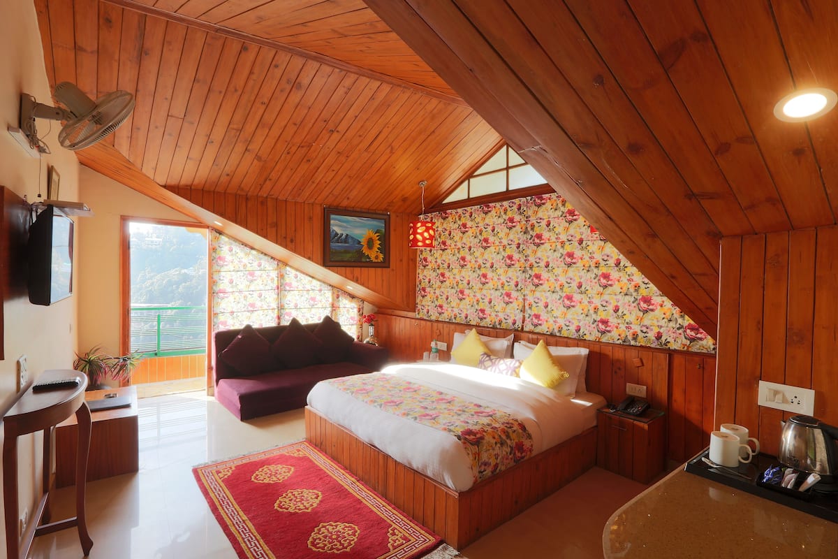 A cozy bedroom with a wooden ceiling, a bed with floral bedding, a red rug, a coffee table, and a view of the outdoors.